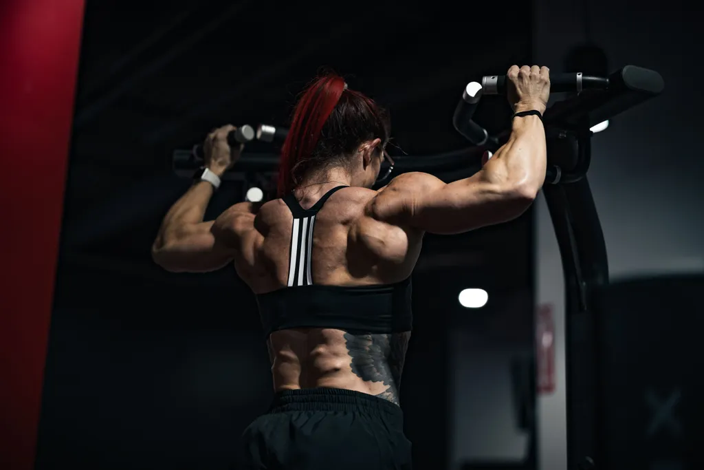 Žena izvodi zgibove na sklopki, detalj leđnih mišića — HIIT trening