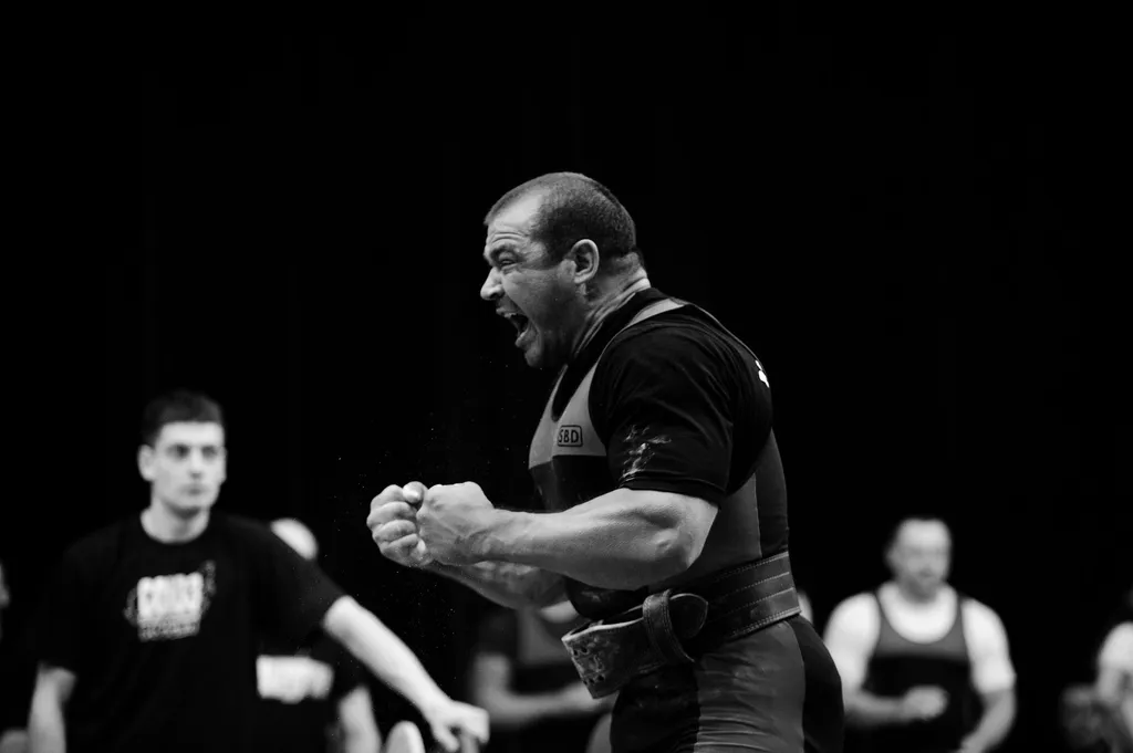 Takmičar slavi uspešno dizanje na powerlifting takmičenju, crno-bela fotografija